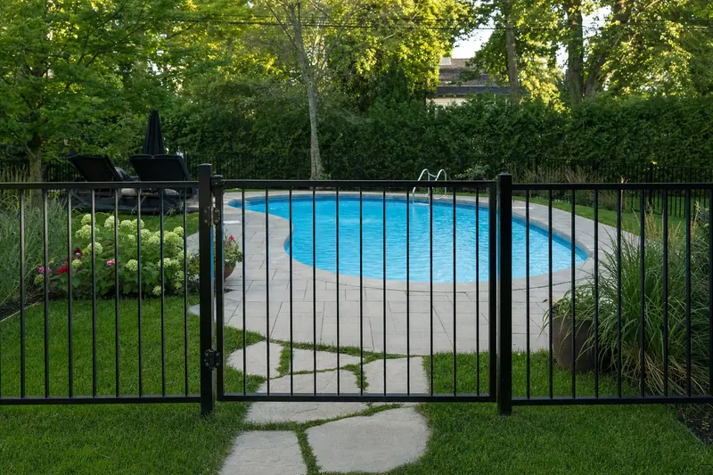 Une piscine creusée entourée d'une clôture d'aluminium noire à barreaux verticaux, avec sa porte fermée